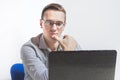 A young businessman in glasses is sitting at a table in the office with a laptop. Looks very thoughtfully at the screen Royalty Free Stock Photo