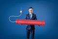 Young businessman holding big red tnt dynamite stick with lighted fuse on blue background