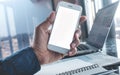 Young businessman holding blank smartphone with workplace.