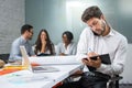 Young businessman holding mobile phone between ear and shoulder talking and writing notes to clipboard in modern office Royalty Free Stock Photo