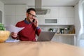 Young businessman holding tax forms and talking over mobile phone with laptop on desk in home office Royalty Free Stock Photo