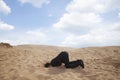 Young businessman kneeling with his head in a hole in the sand