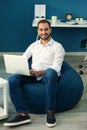 Young businessman with laptop sitting on beanbag chair in office Royalty Free Stock Photo