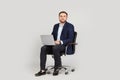 Young businessman with laptop sitting in comfortable office chair on grey background Royalty Free Stock Photo