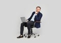 Young businessman with laptop sitting in comfortable office chair on grey background Royalty Free Stock Photo