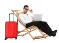 Young businessman with laptop and suitcase on sun lounger against white background. Royalty Free Stock Photo