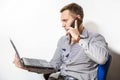 Young businessman with laptop and telephone. He thoughtfully looks  at the screen and speaks on the mobile Royalty Free Stock Photo