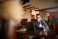 Young businessman looking at camera with laptop in cafe. Smiling man in stylish glasses and smart casual shirt doing his Royalty Free Stock Photo