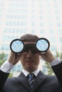 Young Businessman looking into the distance through binoculars with clouds and sky in the lenses of the binoculars Royalty Free Stock Photo