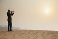 Young businessman looking through telescope in the middle of the desert