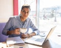 Businessman looks into the frame and drinks cappuccino coffee, next to him lies a notebook with his notes, and a working laptop Royalty Free Stock Photo