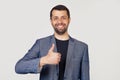 Young businessman man with a beard in a jacket, with a happy smile, shows his thumb to the camera. All is well, it shows success. Royalty Free Stock Photo