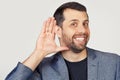 Young businessman man with a beard in a jacket, smiling with his hand above his ear, listening to rumors or gossip. Deafness Royalty Free Stock Photo