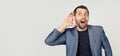 Young businessman man with a beard in a jacket, smiling with his hand above his ear, listening to rumors or gossip. Deafness Royalty Free Stock Photo