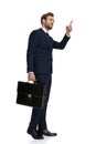 Young businessman in navy blue suit holding suitcase and pointing finger Royalty Free Stock Photo