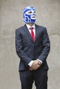 Young businessman in pinstripes suit and wrestling mask looking away over gray background Royalty Free Stock Photo