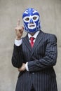 Young businessman in pinstripes suit and wrestling mask pointing up over gray background Royalty Free Stock Photo