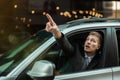 Young businessman pointing with his finger from the open car window, looks amazed, big city life Royalty Free Stock Photo