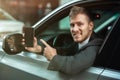 Young businessman pointing with his finger on his smartphone from the open car window, looks happy, big city life Royalty Free Stock Photo