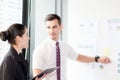 Young businessman pointing towards graph and businesswoman holding clipboard with present profit while giving presentation Royalty Free Stock Photo