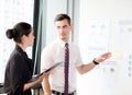 Young businessman pointing towards graph and businesswoman holding clipboard. Royalty Free Stock Photo