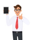 Young businessman showing new tablet computer and making or gesturing thumb up sign. Person holding a digital tab. Male character. Royalty Free Stock Photo