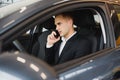 Young businessman sits in luxury car and talks on phone. He looks straight forward. Guy drives car. He holds one hand on steering