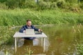 Young businessman sits waist-deep in a swamp at an office desk