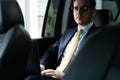 Young businessman sitting on back seat of the car, while his chauffeur is driving automobile.