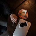 Young businessman is sitting in a cafe at a table with a modern laptop, phone and a cup of hot coffee. Male hand holds an Royalty Free Stock Photo