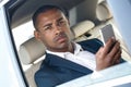 Young businessman sitting in car window opened browsing smartphone looking camera thoughtful close-up