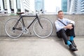 Young businessman sitting on floor with bicycle taking a rest and relaxing on street in urban city Royalty Free Stock Photo