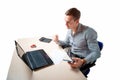 Young businessman sitting at his desk, celebrating success with arms raised while looking at his laptop screen. Isolated on white Royalty Free Stock Photo