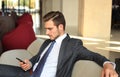Young businessman sitting relaxed on sofa at hotel lobby making a phone call, waiting for someone. Royalty Free Stock Photo