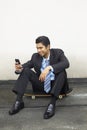 Young businessman sitting on skateboard, text messaging on phone. Conceptual image