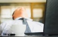 Young businessman is sleeping with a laptop and a coffee cup on the desk. Businessman struggling with drowsiness at workplace