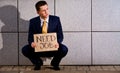 Young businessman squatting with sign Need Job