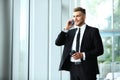 Young businessman standing in an office near the window and talking on a cell phone. Royalty Free Stock Photo