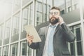 Young businessman is standing outdoor,holding tablet computer and talking on his cell phone. Royalty Free Stock Photo