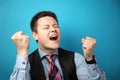 Young businessman in a suit on a blue background celebrating victory and success. Happy and excited expressing