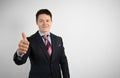 Young businessman in suit on gray background shows his hand thumbs up, symbol of success