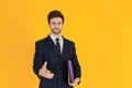 A young businessman in a suit is holding a document file and reach out a hand to hold the hand on the yellow isolated background. Royalty Free Stock Photo