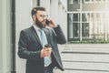 Young businessman in suit and tie is standing outdoor, drinking coffee and talking on his cell phone. Royalty Free Stock Photo