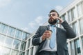 Young businessman in suit and tie is standing outdoor, drinking coffee and talking on his cell phone. Royalty Free Stock Photo