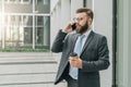 Young businessman in suit and tie is standing outdoor, drinking coffee and talking on his cell phone.Man is working. Royalty Free Stock Photo