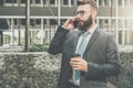 Young businessman in suit and tie is standing outdoor, drinking coffee and talking on his cell phone. Royalty Free Stock Photo