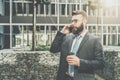 Young businessman in suit and tie is standing outdoor, drinking coffee and talking on his cell phone. Royalty Free Stock Photo