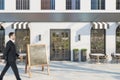 Businessman in suit walking past creative concrete cafe exterior with terrace furniture and empty chalkboard stand in