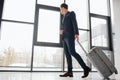 Young businessman in suit walks down hall in airport. He looks at window. Guy rolls suitcase. He looks confident. Royalty Free Stock Photo