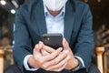 Young Businessman in suit wearing surgical face mask and using smartphone, man typing touchscreen mobile phone in office or cafe. Royalty Free Stock Photo